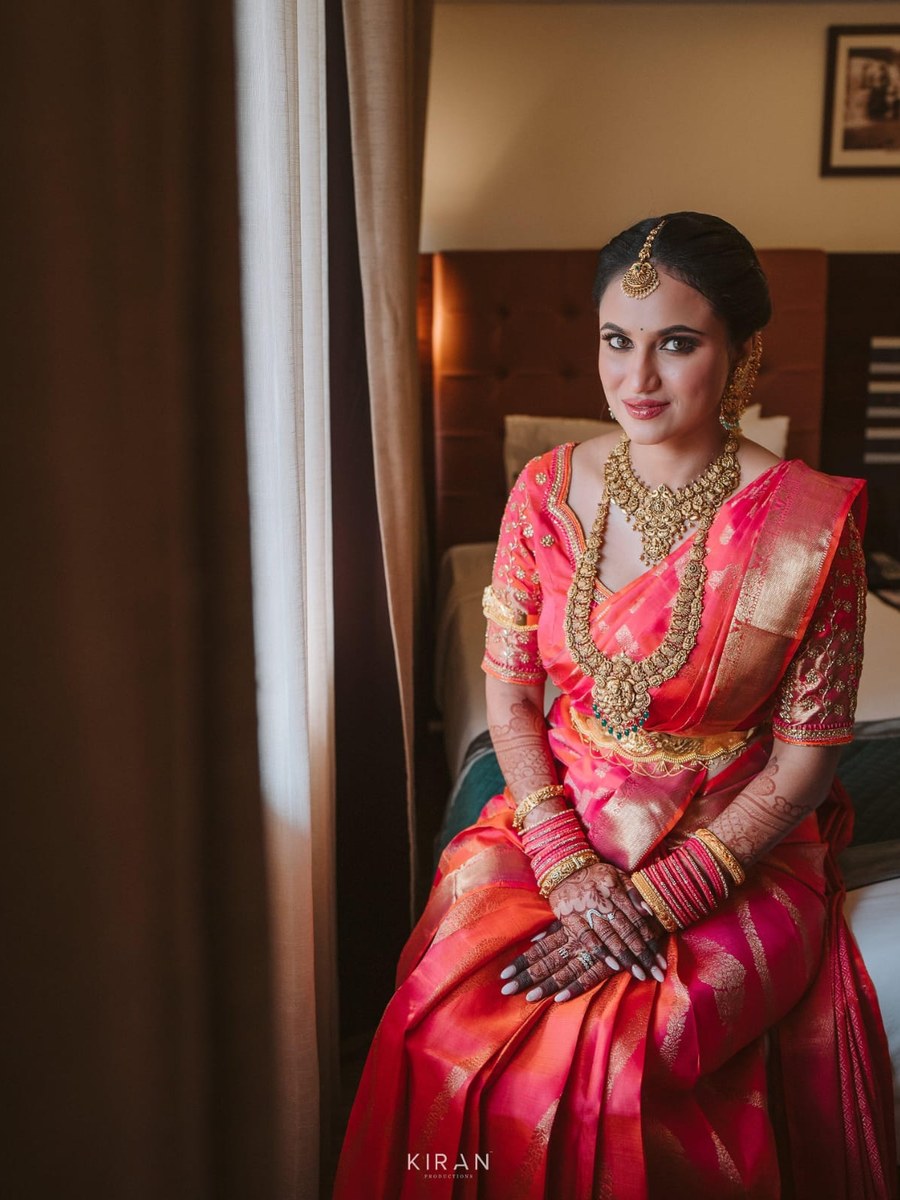 Bride seated in pink-orange silk saree blouse by Hello Beautiful Boutique